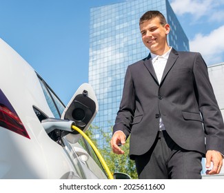 Businessman plugging in the charger in electric car and going to work in business center - skyscraper