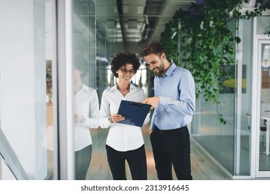 Businessman point with finger on clipboard in hand of his female colleague. Business cooperation and teamwork. Young smiling caucasian millennial colleagues in office. Modern successful people - Powered by Shutterstock