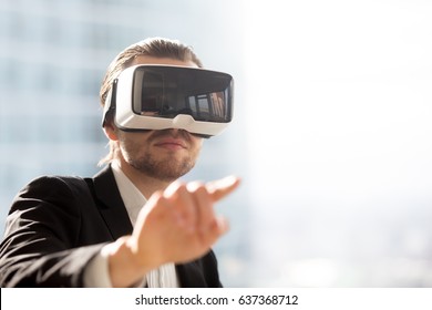 Businessman pointing in air in virtual reality glasses on head. Man in VR headset using gestures in app virtual interface. Male entrepreneur editing project augmented reality, portrait. Copy space   - Powered by Shutterstock