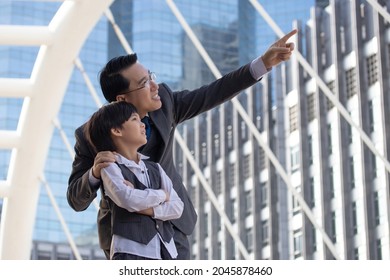 Businessman pointing finger to his property for showing son. Business Father and son confidence Child want to be like a his dad Parent and young boy standing in city with cityscape background.