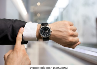 Businessman pointing at hand watch on grey