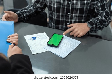 Businessman pointing at a smartphone with green screen on a desk with documents during a business meeting - Powered by Shutterstock