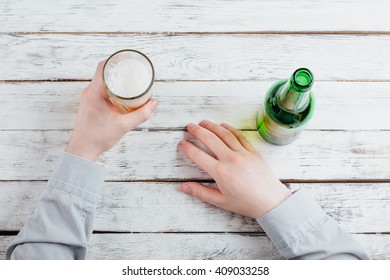 businessman poured beer into a glass from bottle , hands detail on a wooden office table. the work place on background. business and technology concept. desktop top view, unrecognizable people