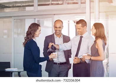 Businessman Pouring Coffee For Collegues In A Meeting Room. Businessmen And Businesswomen Take Coffee Break After Conference. Happy Formal Business Team Drinking Coffee And Relaxing At Work.