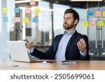 Businessman practicing meditation at desk surrounded by sticky notes and laptop. Focus on stress relief, mindfulness, and mental clarity in busy office environment. Relaxation techniques in workplace