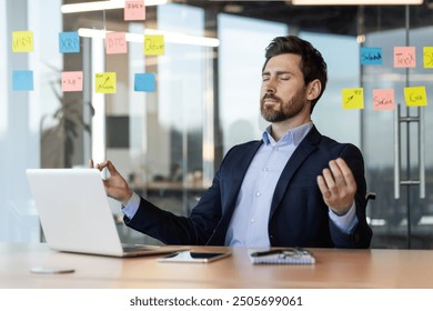 Businessman practicing meditation at desk surrounded by sticky notes and laptop. Focus on stress relief, mindfulness, and mental clarity in busy office environment. Relaxation techniques in workplace - Powered by Shutterstock