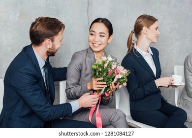 businessman presenting flowers to beautiful asian businesswoman in office