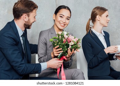 businessman presenting flowers to beautiful smiling asian businesswoman in office