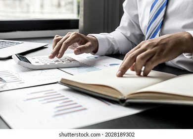 Businessman is pressing a calculator and looking at the information in his notebook, he is checking the balance from the monthly financial and sales documents. Concept of finance and sales management. - Powered by Shutterstock