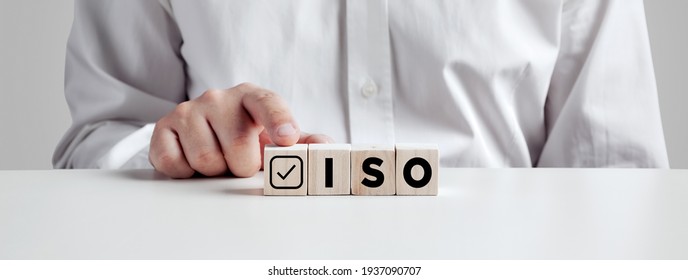 Businessman pressing his finger on the wooden cubes with the abbreviation ISO with check mark. ISO quality control certification concept.