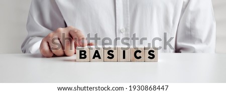 Businessman pressing his finger on the wooden cubes with the word basics. Back to basics, simplification in business or education concept.