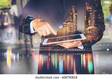 Businessman Pressing  On Virtual Screens Of Ipad, Technology, Internet And Networking Concept .Mix Media With City Scape Twilight.Business Building At Night Life.