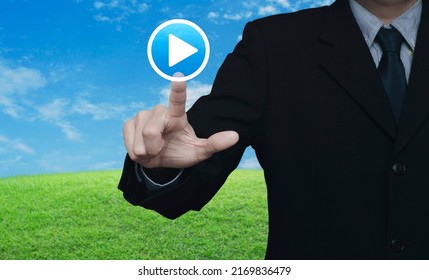 Businessman Pressing Play Button Icon Over Green Grass Field With Blue Sky, Business Music Online Concept