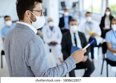 Businessman With Protective Face Mask Holding A Seminar To Large Group Of People In Convention Center.