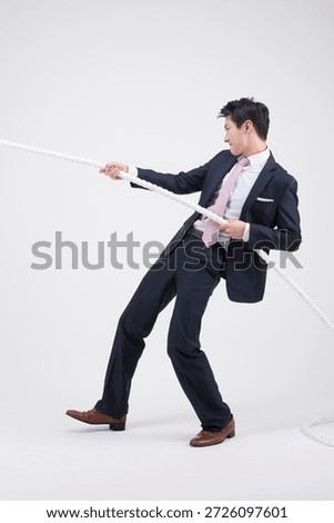 Businessman pulls rope in studio setting while dressed in formal attire during daytime