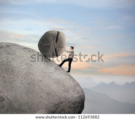 Businessman pushing a boulder on a rock
