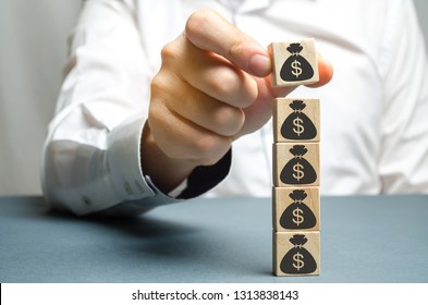 Businessman puts a block with a picture of dollars. Increased budget and profits in the team. The capital accumulation and successful business.Increase investment fund. Saving money. Economic boom - Shutterstock ID 1313838143