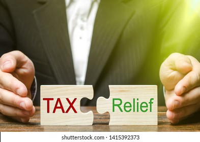 A businessman puts two puzzles with the words Tax and Relief. The concept of reducing the debt burden on business and local production to increase the competitiveness of their products. Economy