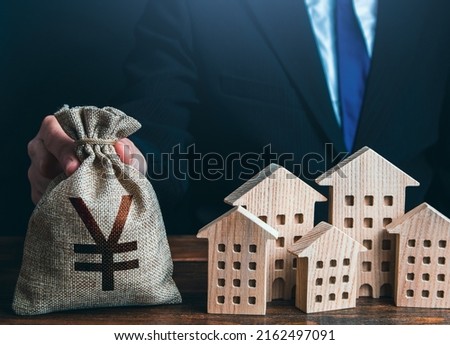 A businessman puts a yuan or yen money bag near the houses. Construction industry, rental business and hotel tourism. Municipal budget of the city. Official. Investments in real estate assets.