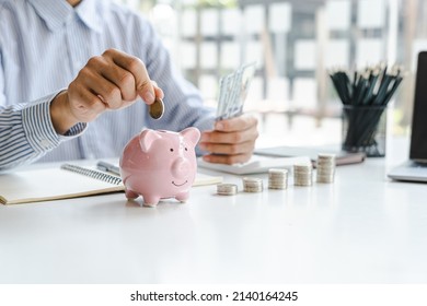 Businessman putting coin into small piggy bank at business desk.