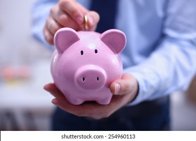 Businessman putting coin into small piggy bank