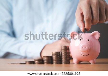 Businessman putting coin to pink piggy bank with increasing coins stacking on table , Money saving and deposit for investment to get profit and dividend concept. 