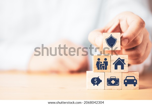 Businessman putting wooden cube block\
stacking with insurance and assurance icon including family health\
real estate car and financial for risk management\
concept.