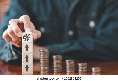 Businessman Putting Wooden Cube Box Target Board With Stack Coins On Desk. Saving Money, Bank Deposits, Interest Collection And Tax Concept. Upward Trend In Business Growth, Financial Management.