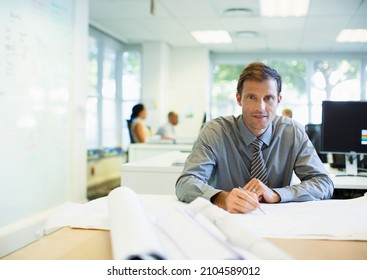 Businessman Reading Blueprints In Office