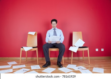 Businessman Reading A Document In A Messy Office Full Of Papers On The Floor