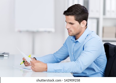 Businessman reading a document while sitting at his desk in the office looking at it with a serious expression