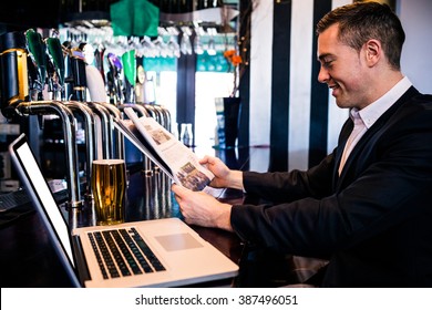 Businessman reading the news and using laptop at the counter in a bar - Powered by Shutterstock