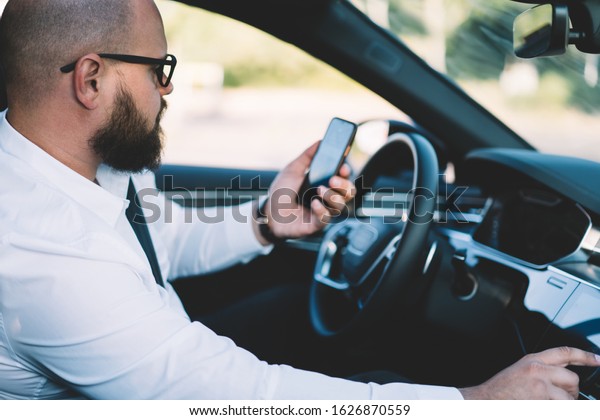 Businessman reading received smartphone\
notification while using self-driving in contemporary car with\
autopilot, male tracking gps location via cellphone application\
connected to 4g\
wireless