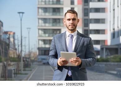 Businessman Or Real Estate Agent Ready To Discuss Business And Stands With Tablet Computer Against New Building