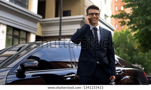 Businessman receiving good news, talking on phone\
near luxury car,\
success