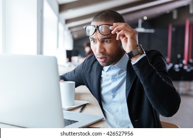 Businessman receiving negative news, touching his glasses, being mad, upset and surprised in front of laptop