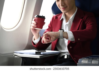 Businessman in a red jacket checking arrival time on his watch while sitting in an airplane seat.