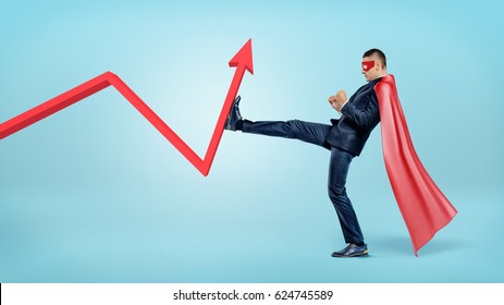 A businessman in a red superhero cape beating a red statistic arrow with his foot. Business and profit. Credit and loss. Financial improvement.