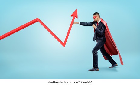A businessman in a red superhero cape throwing punches at a red statistic arrow pointing upwards. Financial results. Fighting for success. Profit and investment.
