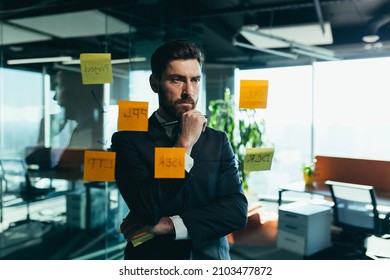 businessman in reflection at a glass task board, hangs plans on colored paper stickers, plans for the near future
