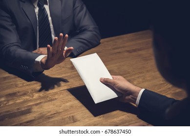 Businessman rejecting money in white envelope offered by his partner in the dark - anti bribery concept