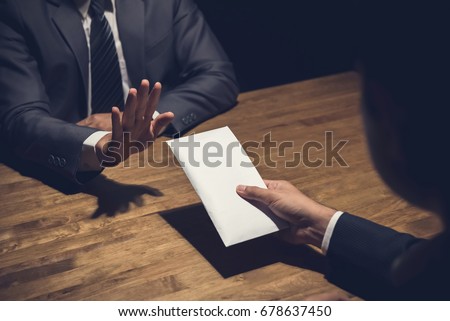 Businessman rejecting money in white envelope offered by his partner in the dark - anti bribery concept