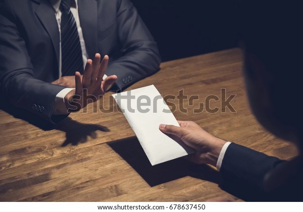 Businessman rejecting money\
in white envelope offered by his partner in the dark - anti bribery\
concept