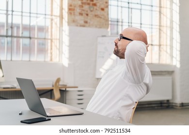 Businessman relaxing at his desk in the office with his hands behind his head staring out of a window - Shutterstock ID 792511534