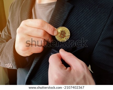 Businessman removing or placing a golden bitcoin in a pocket of his suit jacket in a wide close up view. High quality photo