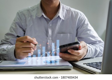 Businessman report graphs and charts of financial statements and profit growth holding a pen and mobile phone at desk.Business concept of digital communication technology