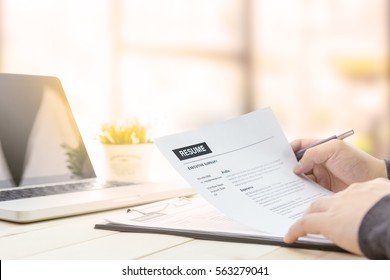 Businessman Review His Resume On His Wooden Desk Before Sending To Find A Job With Laptop Computer, Clock And Glasses.