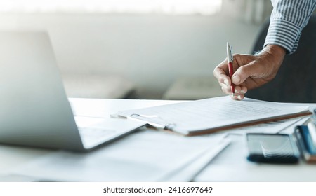 Businessman reviewing document reports at office workplace with computer laptop. legal expert, professional lawyer reading and checking documents or insurance contract before sign, close-up shot - Powered by Shutterstock