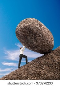 Businessman Rolling Up Giant Boulder On Slope Over Blue Sky