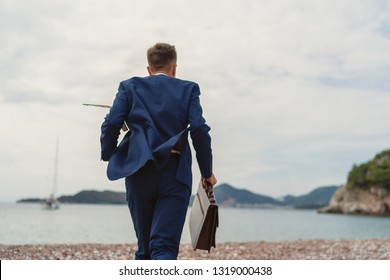 Businessman running to the sea holding in hand briefcase. Back view - Powered by Shutterstock